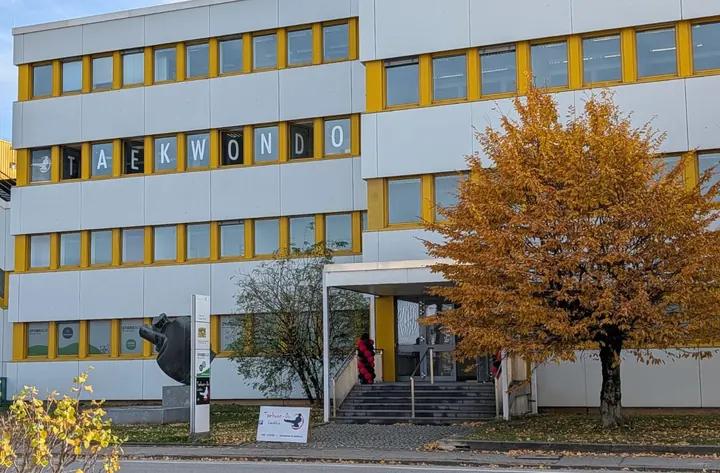 Bürogebäude Siemensstraße 20 im Herbst mit dem Schriftzug TAEKWONDO in den Fenstern im 2. Stock, davor ein Baum mit gelbem Laub und der Eingang mit Treppe