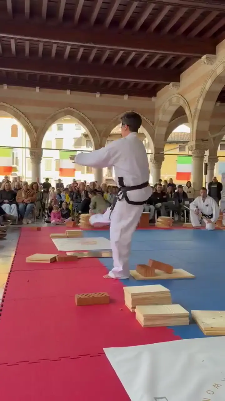 Vorführung einer Form unter den Bögen der Loggia del Lionello in Udine, Schwarzgurt im weißen Anzug vor Publikum